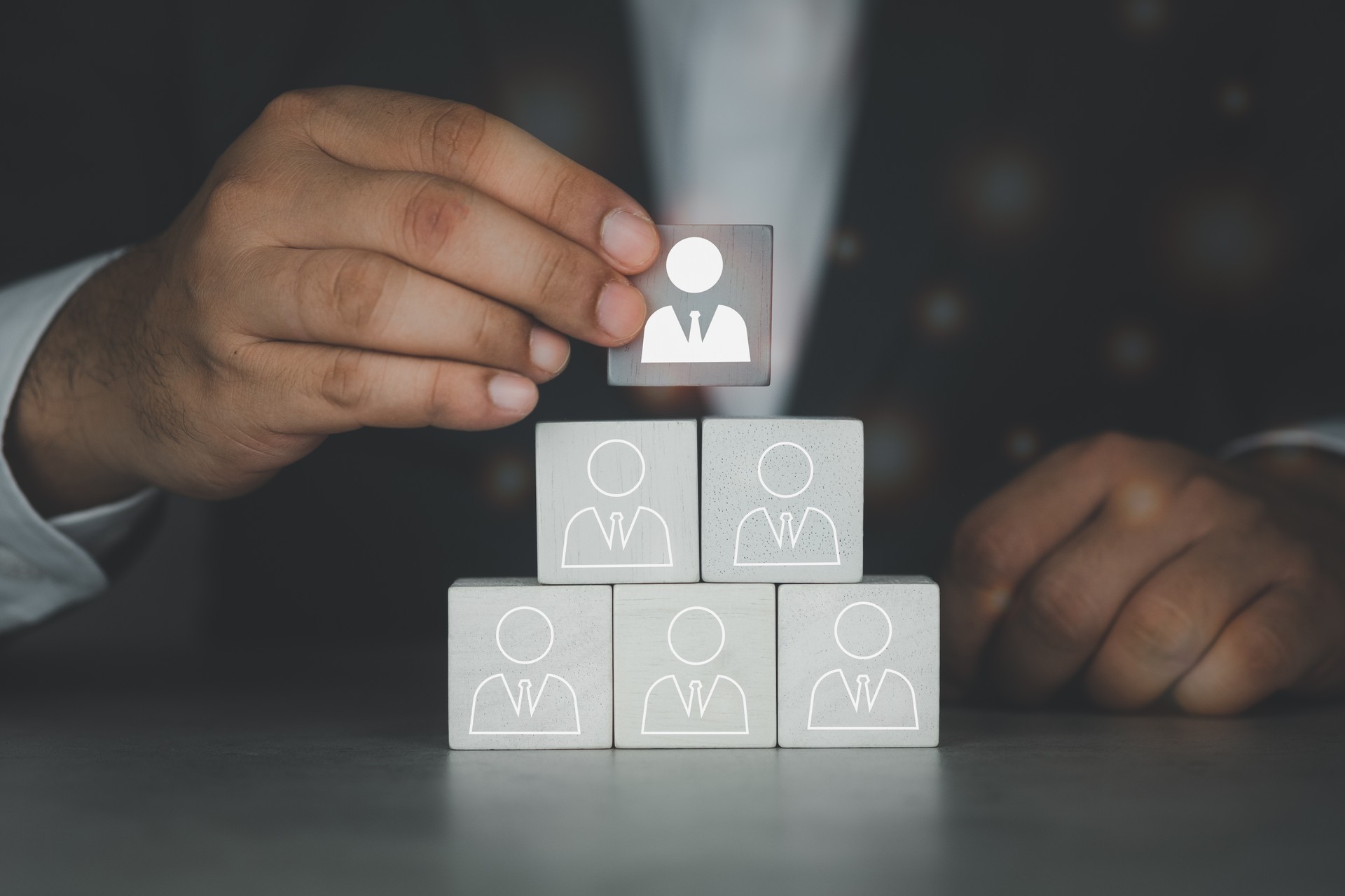 Businessman hand putting wood cube block leader icon on top pyramid. The concept of resource human resources management.